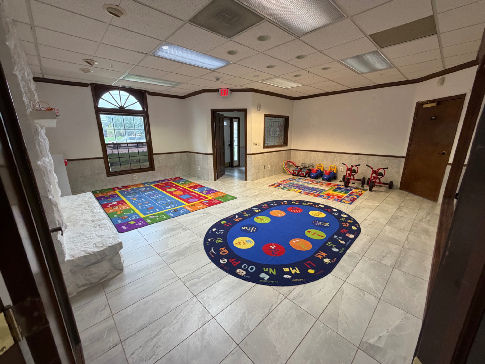 Large activity room with colorful rugs and ride-on toys